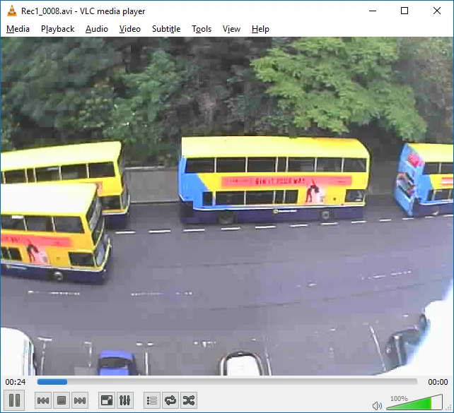 CCTV footage of buses on a road, with trees moving in the wind across the top half of the frame.