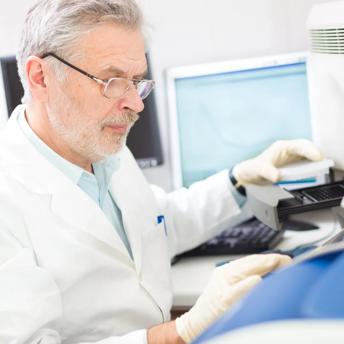 A scientist in a white coat and gloves working at a laboratory workstation.