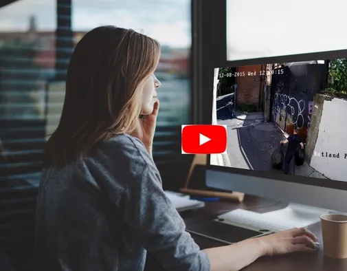 An analyst at a desk reviewing timestamped CCTV footage of an alleyway on a monitor.