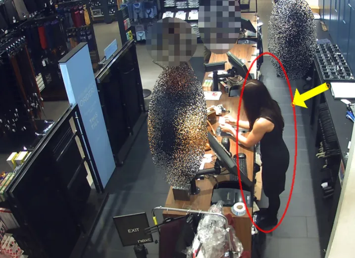 High quality CCTV still in a shop. Several people are blurred out entirely, while one woman at the counter is circled in red and marked with an arrow.