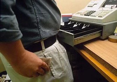 Close-up of a cashier at an open till slipping a banknote into their apron pocket.